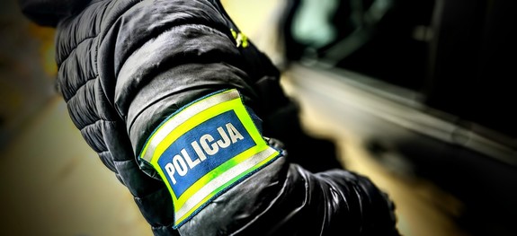 Ramię policjanta na którym znajduje się opaska z napisem: Policja.