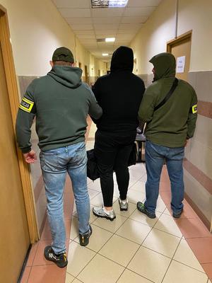 Dwaj funkcjonariusze prowadzą zatrzymanego.