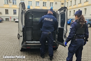 Dwoje policjantów zamyka kratę w policyjnym radiowozie, w którym siedzi zatrzymany.
