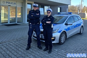 Policjant i policjantka stoją przy radiowozie.