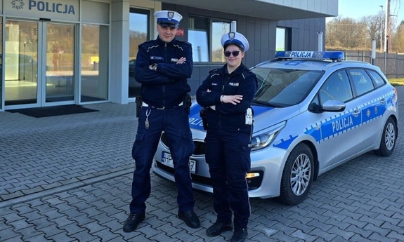 Policjant i policjantka stoją przy radiowozie.