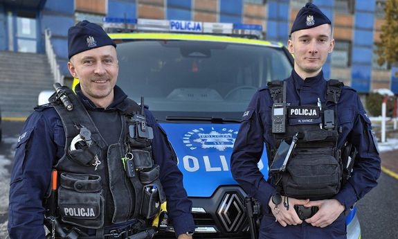policjanci stoją przed radiowozem.