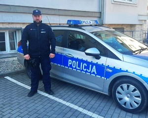 Umundurowany policjant stoi przy radiowozie.