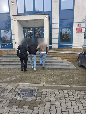Nieumundurowani policjanci prowadzą mężczyznę do prokuratury.