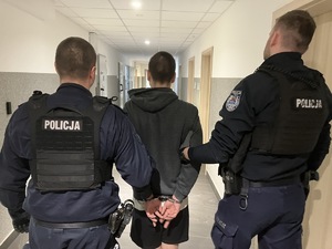Dwaj umundurowani policjanci prowadzą korytarzem zatrzymanego mężczyznę.