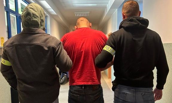 Dwaj nieumundurowani policjanci prowadzą korytarzem zatrzymanego.