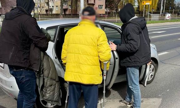 Zatrzymany przy policyjnym nieoznakowanym radiowozie. Przy nim po bokach stoją dwaj nieumundurowani policjanci.