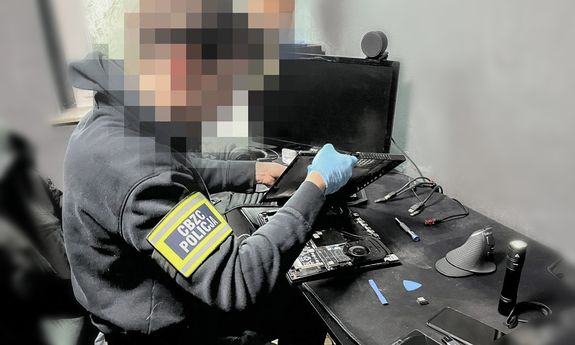policjant siedzi przy komputerze i go rozbiera.