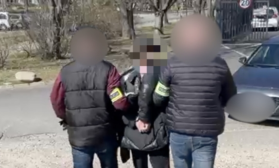 Dwaj funkcjonariusze prowadzą zatrzymaną osobę w kierunku nieoznakowanego radiowozu.