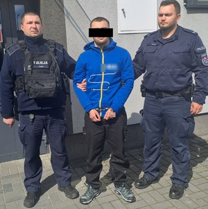 Zatrzymany mężczyzna w kajdankach trzymany przez dwóch policjantów.