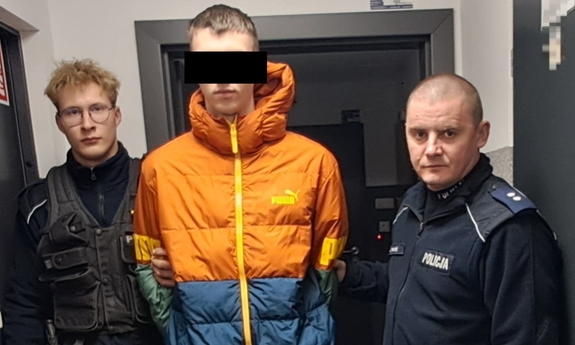 Zatrzymany mężczyzna w kajdankach trzymany przez dwóch policjantów.