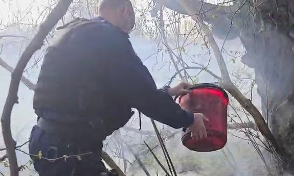 Na zdjęciu policjant w trakcie akcji gaśniczej płonącej trawy.