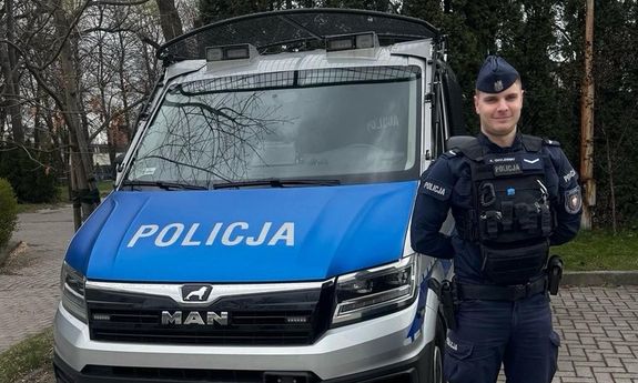 policjant stoi przed radiowozem.