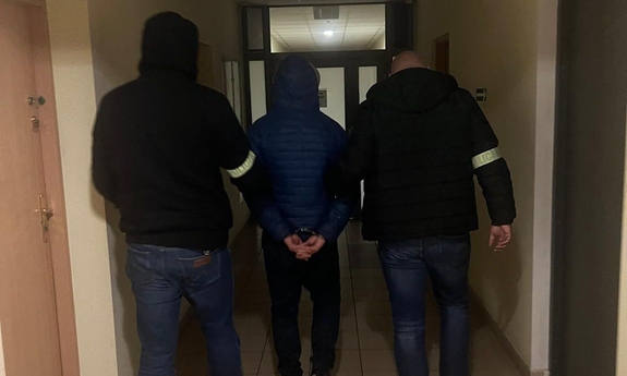Policjanci prowadzą zatrzymanego mężczyznę w kajdankach.