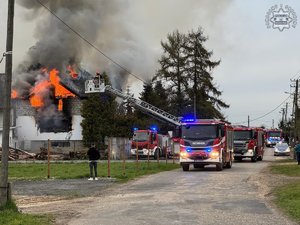 Palący się budynek a przy nim wozy strażackie, z boku widać również radiowóz.