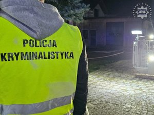 Plecy policjanta w żółtej kamizelce z napisem: Policja Kryminalistyka.