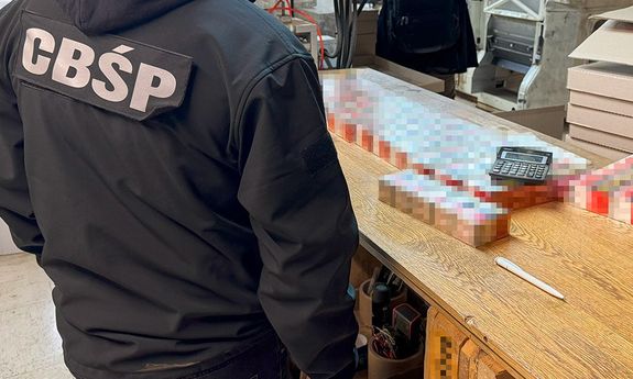 policjant z CBŚP stoi przed stołem z zarekwirowanymi papierosami.