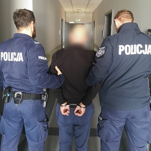 Dwaj funkcjonariusze z zatrzymanym mężczyzną zakutym w kajdanki.