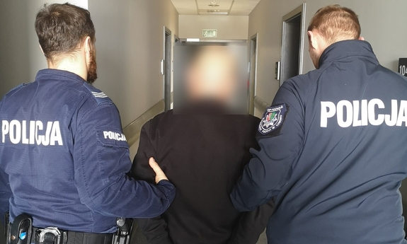 Dwaj funkcjonariusze z zatrzymanym mężczyzną zakutym w kajdanki.