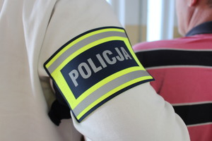 Na ramieniu funkcjonariusza opaska z napisem Policja.