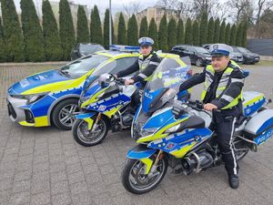 Dwaj funkcjonariusze na motocyklach na parkingu stojące przy radiowozie.
