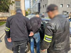 Dwaj funkcjonariusze prowadzą zatrzymanego w kajdankach.