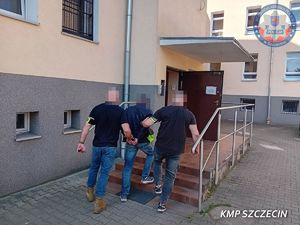 dwóch policjantów prowadzi zatrzymanego do budynku.