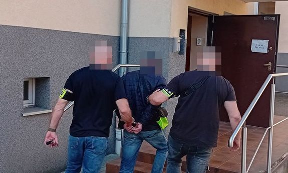 dwóch policjantów prowadzi zatrzymanego do budynku.