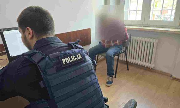 policjant siedzi przy biurku, obok siedzi zatrzymany.