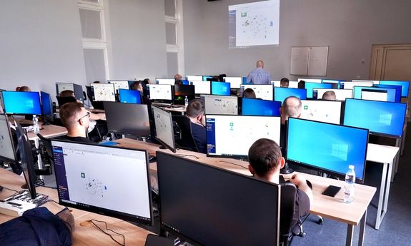 policjanci siedzą w ławkach przed komputerami.