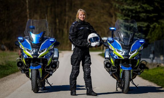 na drodze stoją dwa motocykle, pomiędzy nimi stoi policjantka w stroju motocyklowym.