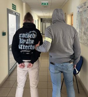 Policjant z zatrzymanym mężczyzną zakutym w kajdanki.