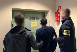 Na zdjęciu policjanci prowadzą zatrzymanego mężczyznę w kajdankach.