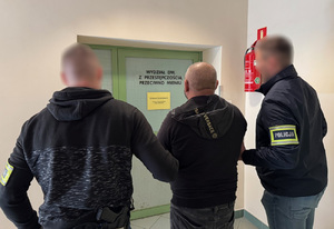 Na zdjęciu policjanci prowadzą zatrzymanego mężczyznę w kajdankach.