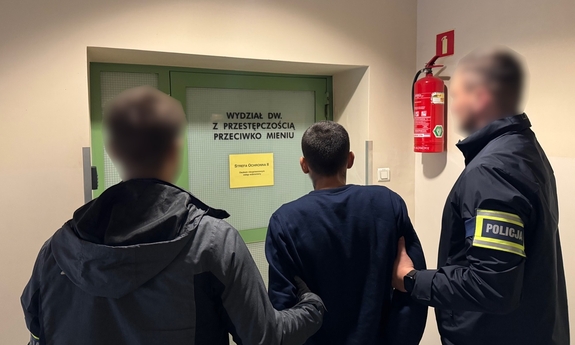 Na zdjęciu policjanci prowadzą zatrzymanego mężczyznę w kajdankach.