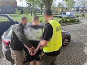 Dwaj funkcjonariusze prowadzą zatrzymanego mężczyznę zakutego w kajdanki.