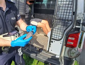 policjant stoi obok radiowozu gdzie jest zatrzymany.
