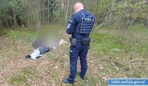 Policjant przy odnalezionym mężczyźnie leżącym na ziemi.