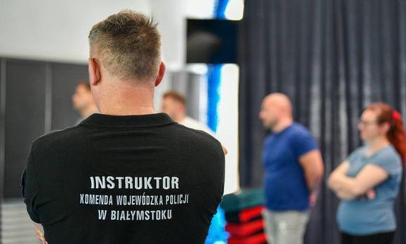 Stojący tyłem instruktor na którego plecach widać napis: instruktor Komendy Wojewódzkiej Policji w Białymstoku, a przed nim ratownicy medyczni.