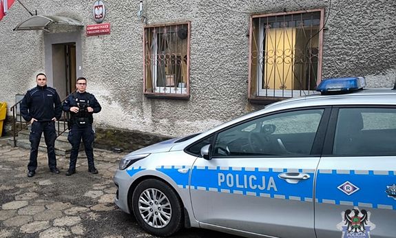 Policjanci w mundurach stoją obok radiowozu.
