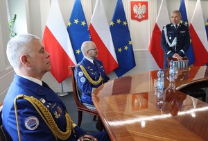 Uczestnicy uroczystości siedzą przy stole. I zastępca komendanta głównego Policji nadinspr. Roman Kuster przemawia.