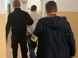 Dwaj nieumundurowani policjanci prowadzą korytarzem zatrzymanego. Widok z tyłu.