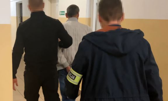 Dwaj nieumundurowani policjanci prowadzą korytarzem zatrzymanego. Widok z tyłu.