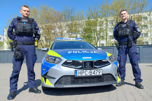 Dwaj policjanci stoją przy radiowozie.