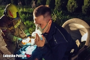 Policjant w masce ratowniczej, obok strażak.