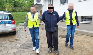 Dwaj policjanci prowadzą zatrzymanego mężczyznę zakutego w kajdanki.
