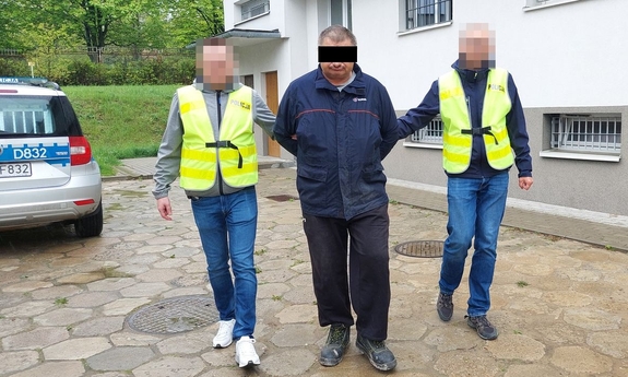 Dwaj policjanci prowadzą zatrzymanego mężczyznę zakutego w kajdanki.