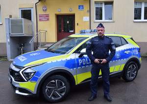 Policjant stoi przy radiowozie.