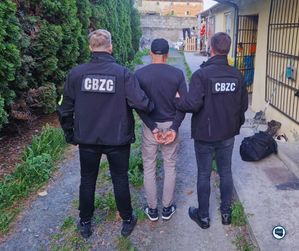 Dwóch policjantów prowadzi zatrzymanego mężczyznę.