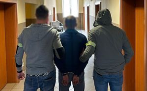 Dwaj policjanci z zatrzymanym mężczyzną zakutym w kajdanki.